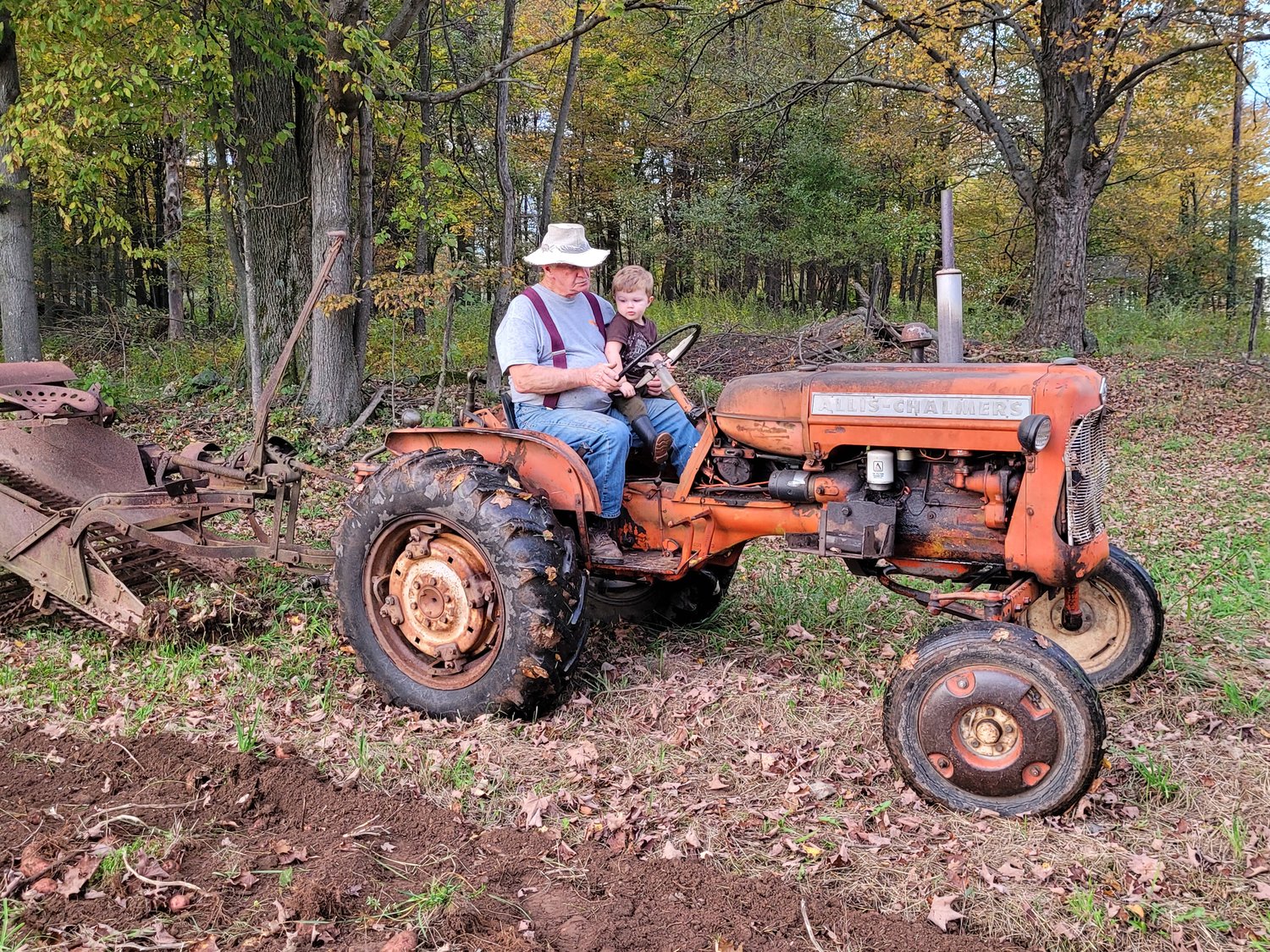 Rorick sits on the tractor, harvesting potatoes with his grandpa.